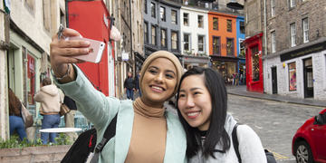 Two students taking selfie in front of colourful Edinburgh buildings