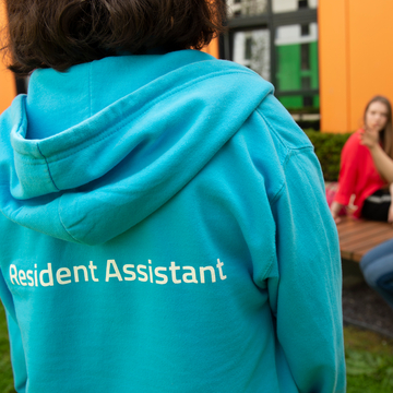 Resident Assistant wearing blue hoodie with 'Resident Assistant' on the back