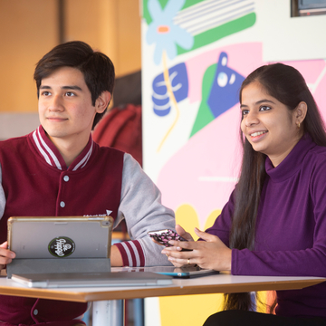 Two students working together with a laptop and tablet in Bainfield Common Room