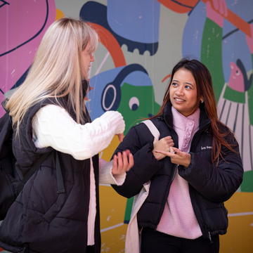Two students talking to each other in front of the painted mural at the entrance to Bainfield student accommodation