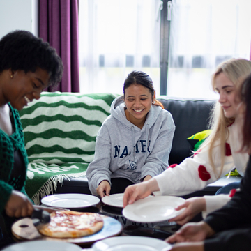 Three students sharing pizza in the lounge of a student accommodation flat