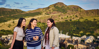 Three students laughing and enjoying a walk in front of Arthur's Seat in Edinburgh