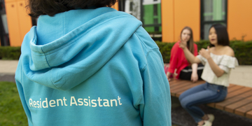 Close up of student accommodation resident assistant, wearing a blue hoodie with 'Resident Assistant' on the back