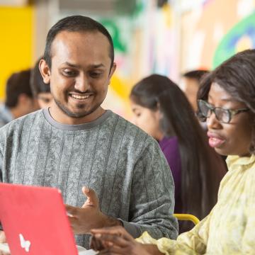 Two students looking at a laptop together in a bright colourful room
