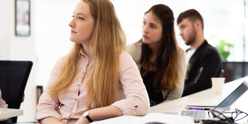 Three students sitting at a desk listening to a presentation