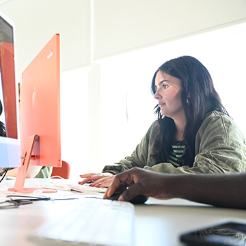 Student sitting in a bright computer suite working at a screen