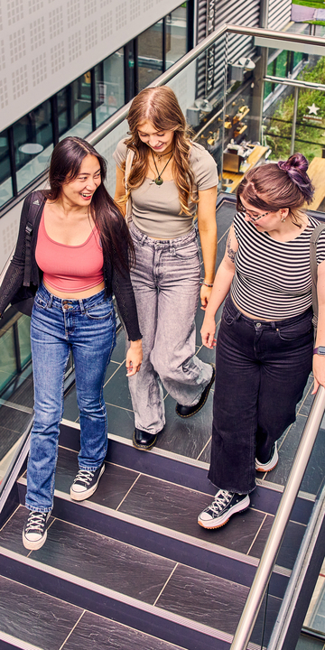 Three students smiling and talking as they walk down the stairs on campus