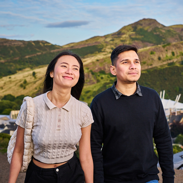 Two students walking together on a sunny day, with hills in the background