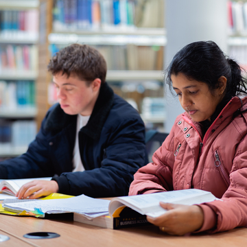 Two students reading over notes together in the library
