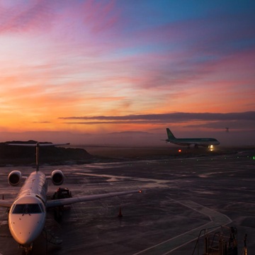 Two planes sitting on the airport tarmac at sunset