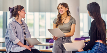 Three students talking with each other and looking over papers