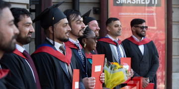 A group of students in graduation robes, standing for a photo holding their certificates