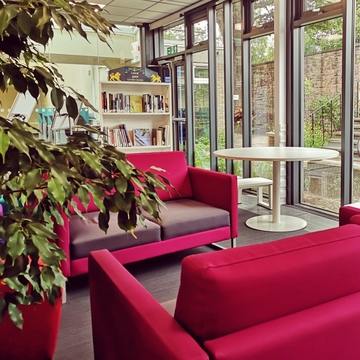 Merchiston library relaxation space. two red sofas in front of a bookcase, situated beside windows looking out onto a small walled garden.