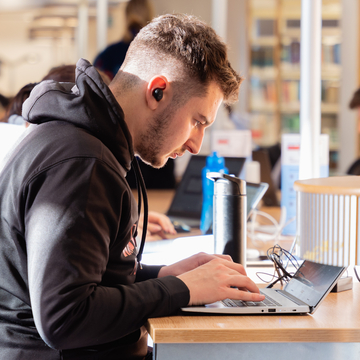 Student sitting at a desk in the library, looking at a laptop screen