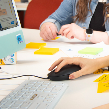Close up of two students' hands as they work at a desk with post-it notes, a keyboard and mouse