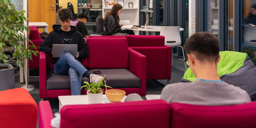 Students sitting on sofas in library, working on laptops