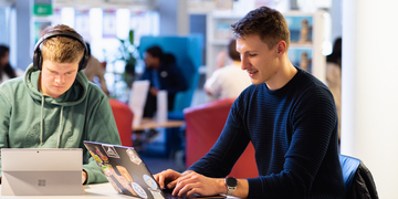 Two students working in the library with their laptops