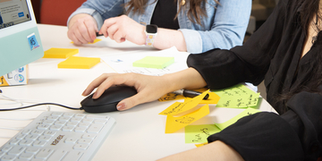 Close up of students working at a library desk with post-its, keyboard and mouse