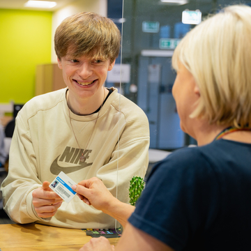 Student getting assistance from member of staff at helpdesk, who is handing back their student card