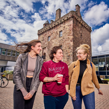 Three students in Edinburgh Napier hoodies walking together in front of Merchiston tower