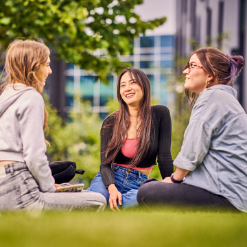 Three students sitting chatting on the grass outside Sighthill campus