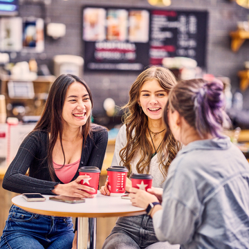 Three students sitting and chatting in a campus cafe with coffee cups