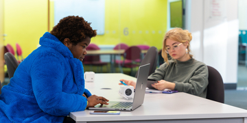 Two students working on laptops near one of the study spaces on campus