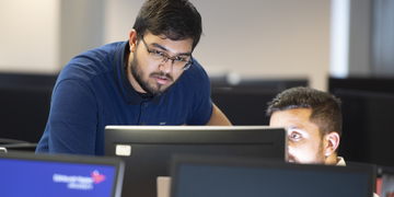 Student standing over a computer screen, getting assistance