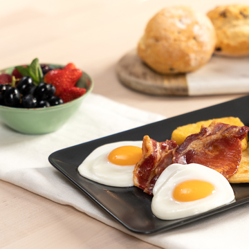 Tray of breakfast items including fruit, scones, bacon, egg and potato scone