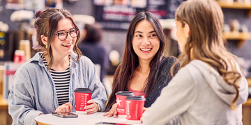 Three students sitting in a cafe on campus, each with red coffee cups
