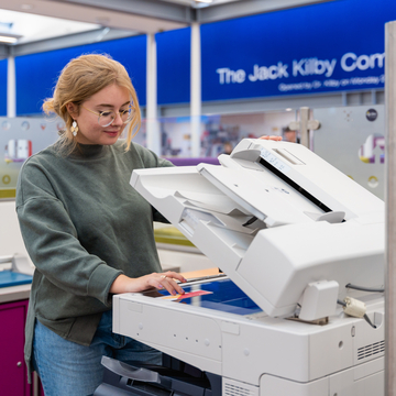 A student standing in front of the printers, using it to scan a piece of paper