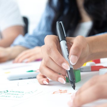 Close-up of hands holding a pen and drawing on a sheet of paper