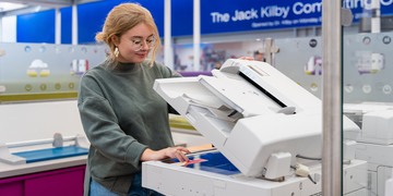 A student standing in front of the printers, using it to scan a piece of paper