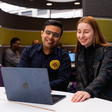Two students sitting in the library area looking at a laptop screen together