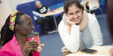 Two students smiling and talking at a table with coffee