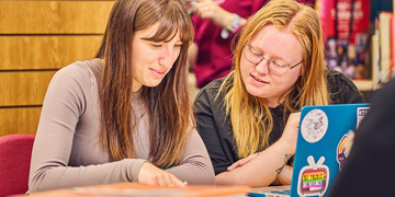 Two students looking over notes next to an open laptop in the library