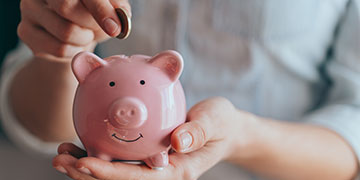 A person depositing a coin into a pink piggybank