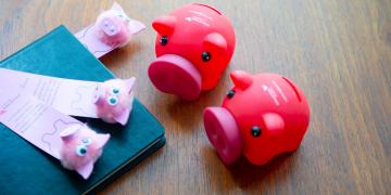 Two red Edinburgh Napier branded piggy banks next to a notebook and some pig-themed bookmarks
