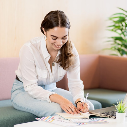 Student sitting at a desk with a laptop, writing in a notebook