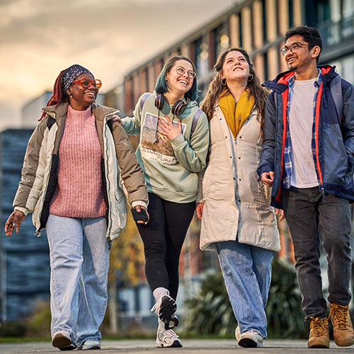 Four students smiling and walking together in the late afternoon with Bainfield student accommodation in the background