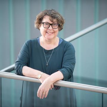 Professor Sue Rigby, Principal of Edinburgh Napier University, smiling as she stands next to a balcony in the atrium