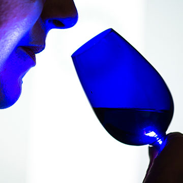Close-up image of a person holding a wine glass to their face, with a blue glowing light over the person and the glass