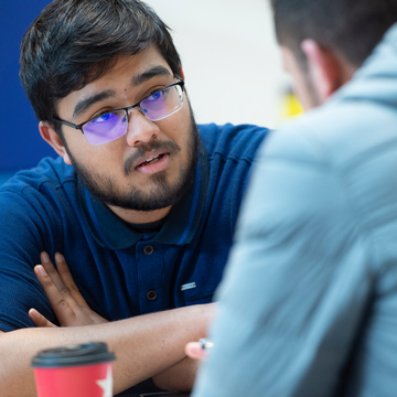 A student sitting in conversation with someone else, a coffee cup in the foreground