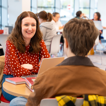 Two students sitting in library area, smiling and talking to each other