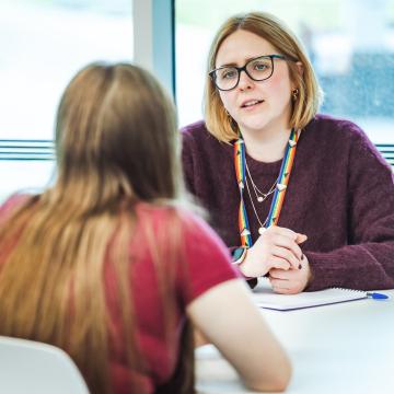 A staff member in supportive conversation with a student at a table