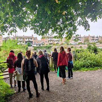 A group of students under a green canopy of trees looking out over the view of the city on a nature wellbeing walk