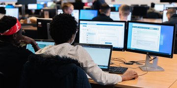 Student sitting at computer in computer suite, looking at information on the screen