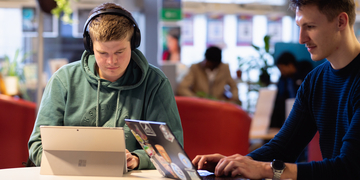 Two students studying at a table with headphones on