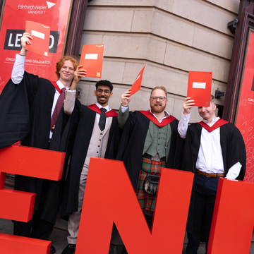Graduating students wearing their graduation gowns outside the Usher Hall in Edinburgh, standing next to giant 'ENU' red letters