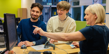 Two students getting assistance on a computer by a member of university staff